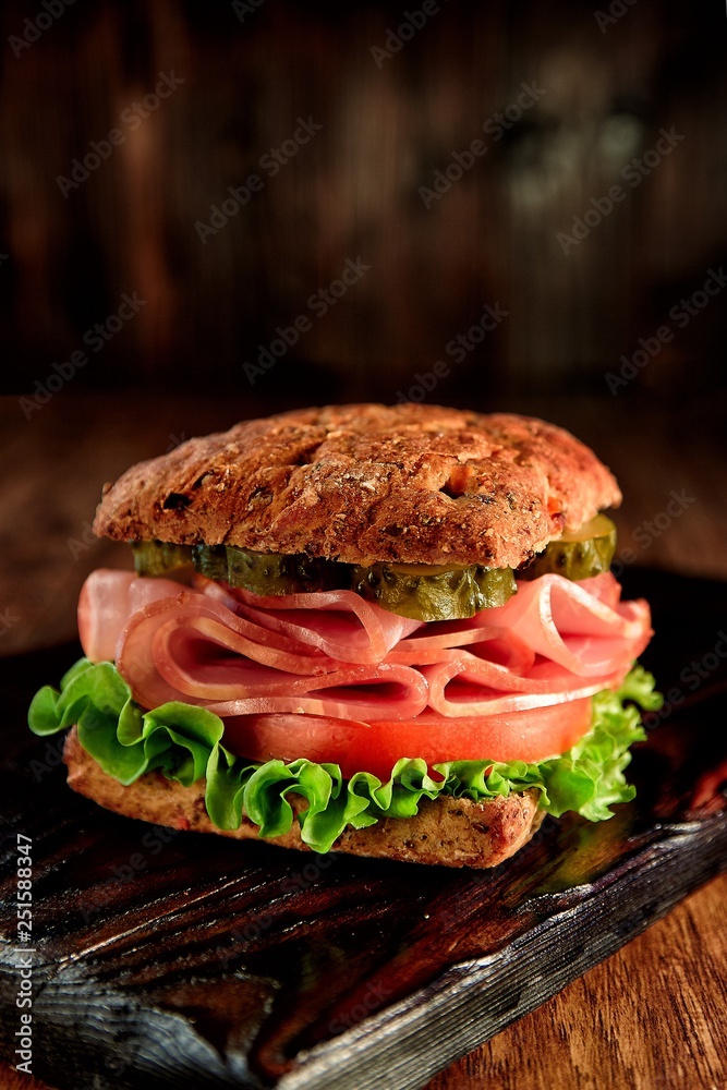 resh sandwich with ham, cheese, bacon, tomatoes, salad, cucumbers and onions on a wooden cutting Board