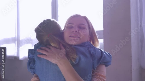 maternal tenderness, little daughter rushes into mother arms and gives big hug at home against window in sun rays close-up
