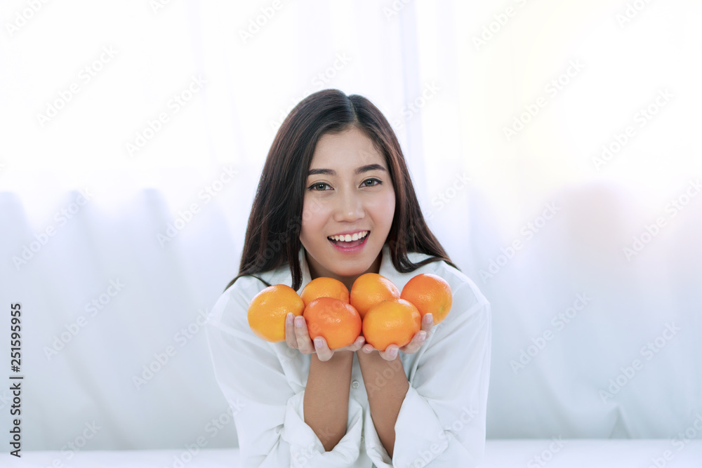 Lifestyle and healthy food concept. Happy young woman holding fresh oranges fruit in her hand on white bed at home with copy space. Lifestyle and healthy food concept. Happy young woman holding fresh oranges fruit in her hand on white bed at home with copy space.