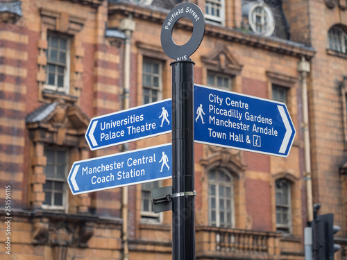 Street sign on Fairfield street indicating City Center, Piccadilly Gardens and Universities Palace Theatre. Typical architecture in the background.