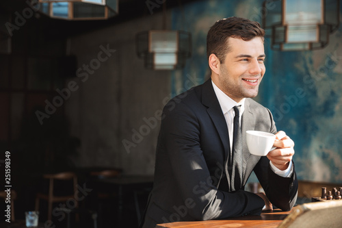 Handsome happy young businessman sitting in cafe drinking coffee.