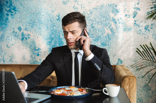 Businessman sitting in cafe using laptop computer have a breakfast or dinner eat talking by phone.