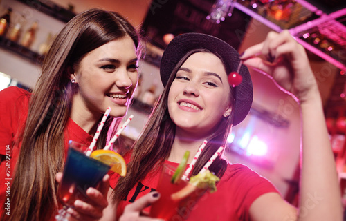 two lesbian girlfriends feed each other cherries with a cocktail in the background of a bar in a nightclub. LGBT
