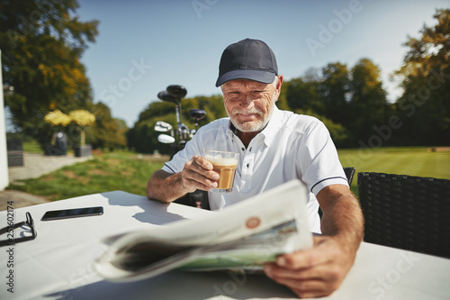 Bild auf Leinwand Smiling senior man drinking coffee after a round of golf