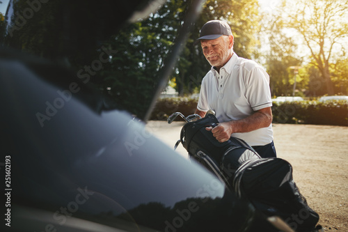 Schilderij op canvas Senior man packing his golf clubs in a car trunk