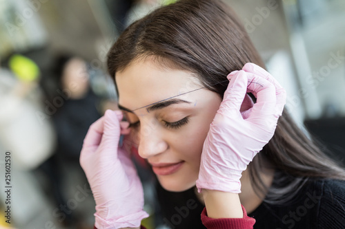 Beautiful young girl with long eyelashes tweezing her eyebrows in a beauty salon. Eyebrow Correction. Beauty Concept. Permanent Makeup. Microblading brow. Beautician Doing brows Tattooing. Treatment.