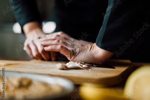 Chef crushing garlic with knife on a wooden board