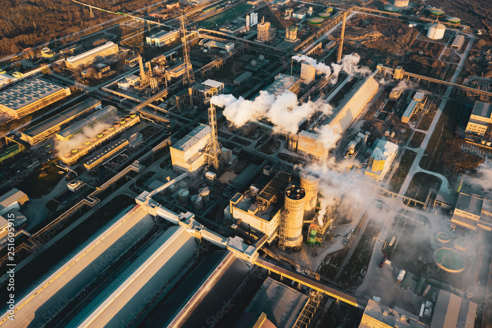 Aerial view, the vast territory of a large industrial chemical plant with high pipes in the bright light of winter sunset. Thick smoke comes from a high pipe. Environmental pollution. Drone
