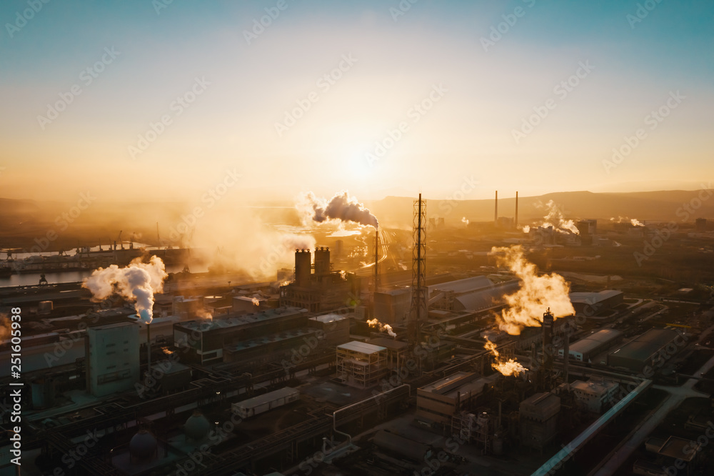 Fototapeta premium Aerial view, the vast territory of a large industrial chemical plant with high pipes in the bright light of winter sunset. Thick smoke comes from a high pipe. Environmental pollution. Drone