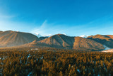 Bright panorama of mountain ranges with snow on the tops against the blue sky in winter. High mountains in the sun. Green hills and dense forests. Pine forests. Relax. Drone