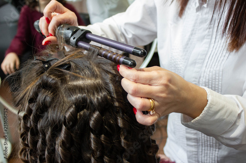  a hairdresser master in the salon does her hair curly with curling iron