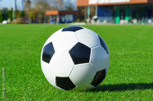 Classic soccer ball lying on the bright green grass on the football field in the background of the stands for the fans at the sports stadium close-up in a large sports center for football players 