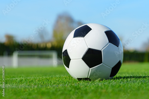 Classic soccer ball lying on the bright green grass on the football field in the background of the stands for the fans at the sports stadium close-up in a large sports center for football players