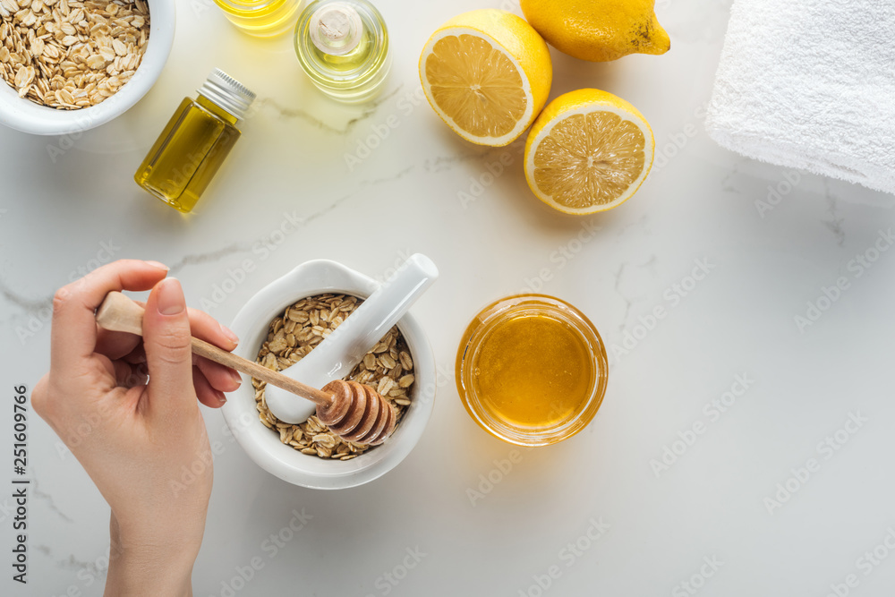 cropped view of woman adding honey into pounder with oat flakes on white surface cropped view of woman adding honey into pounder with oat flakes on white surface