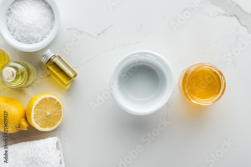 top view of lemons and bowls with different ingredients for homemade cosmetics on white surface