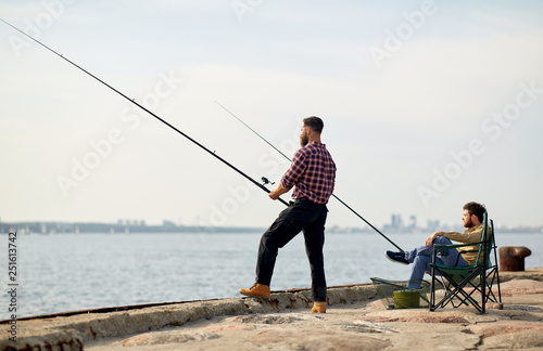 leisure and people concept - happy friends with fishing rods on pier at sea