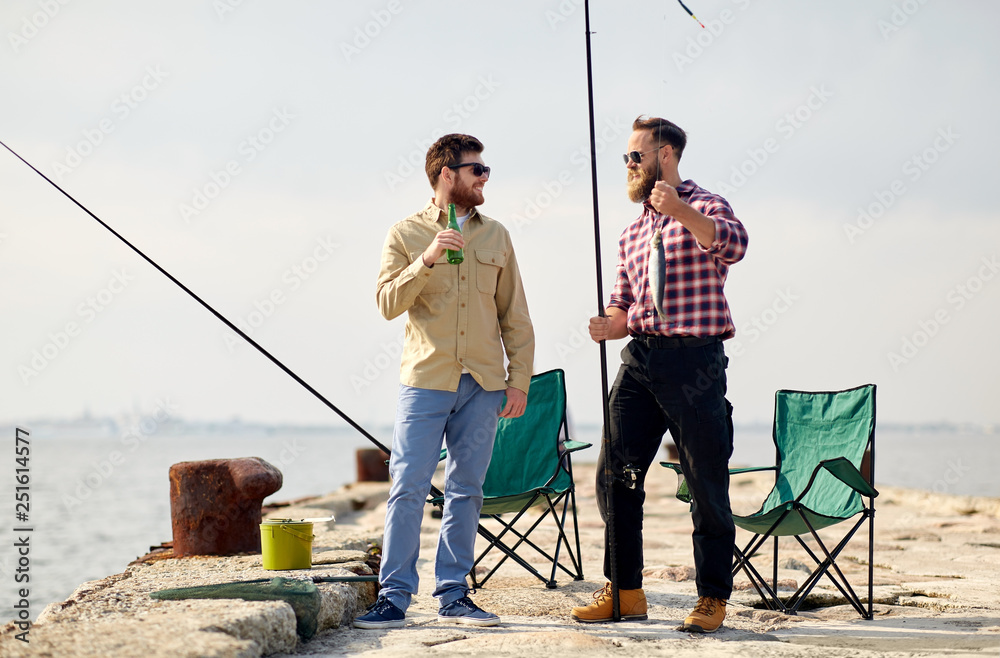leisure and people concept - happy friends with fishing rods, fish and beer talking on pier at sea leisure and people concept - happy friends with fishing rods, fish and beer talking on pier at sea