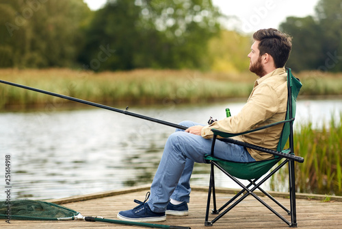 leisure and people concept - bearded fisherman with fishing rod at lake