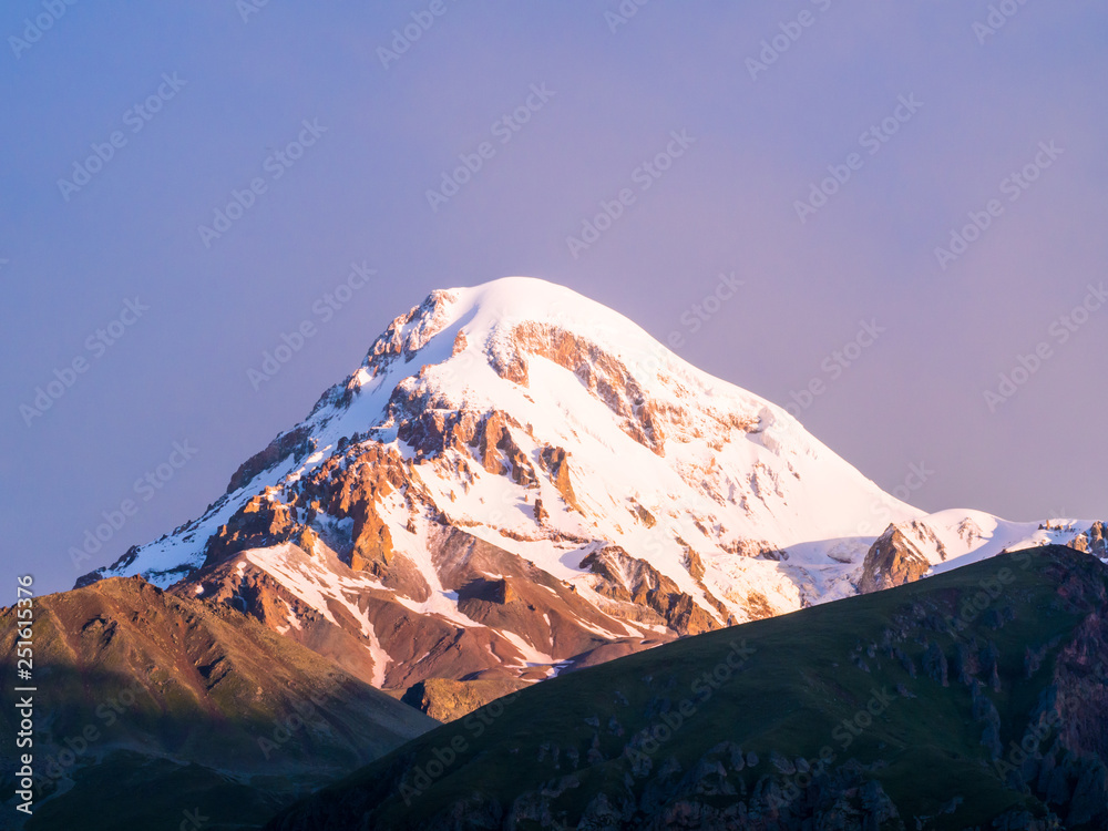 Mount Kazbek in the Republic of Georgia, Caucasus, at sunrise, seen from the Gergeti Trinity Church. Horizontal / landscape orientation, purple early morning sky in the background. 