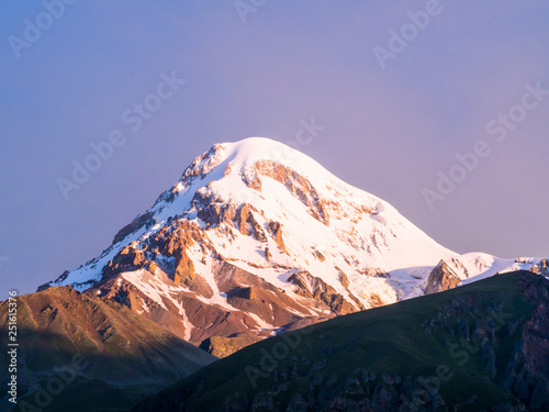 Mount Kazbek in the Republic of Georgia, Caucasus, at sunrise, seen from the Gergeti Trinity Church. Horizontal / landscape orientation, purple early morning sky in the background. 