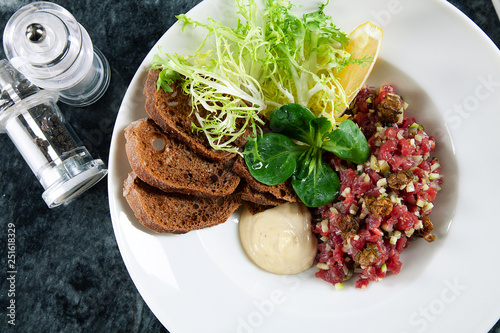 Close up view on served Steak beef tartare served with lemon, bread, sauce and salad on marble table. Restaurant food menu, recipe photo with copy space. Delicious flat lay food. European cuisine