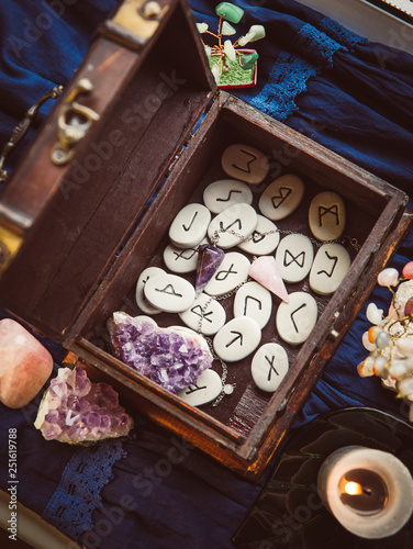  Clairvoyant tools rune stones, crystal pendulums in natural dark wooden case box on dark blue background. © FotoHelin