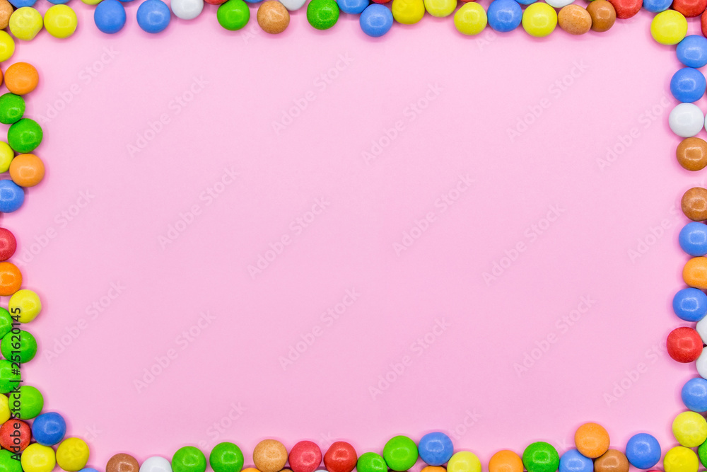 A frame of colorful chocolates. Close-up view of the top, pink background. A frame of colorful chocolates. Close-up view of the top, pink background.