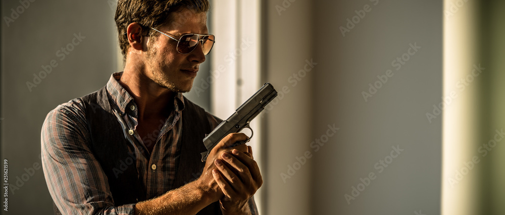 Young Caucasian male holding a gun in a sunset hotel - obrazy, fototapety, plakaty 