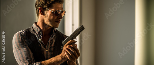 Young Caucasian male holding a gun in a sunset hotel
