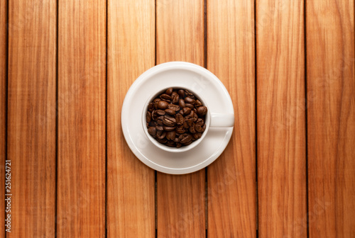 Top view photo of a coffee cup filled with coffee beans and saucer over a wood table background