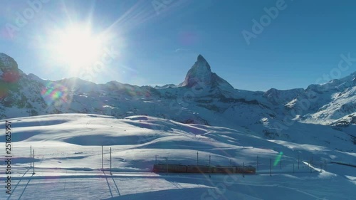 Matterhorn Mountain and Cog Railway Train in Sunny Winter Day. Swiss Alps. Switzerland. Aerial View. Drone Flies Sideways photo