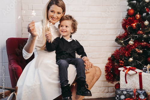 Smiling mother and son hold sparklers at home during Christmas