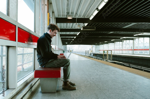 Side view of man using laptop while sitting on railway platform