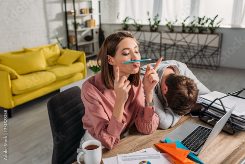 Obraz na płótnie funny girlfriend sitting near boyfriend sleeping at desk near laptop and cup wit