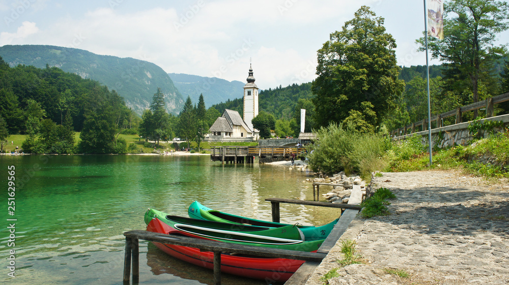 Picturesque view of the Church of St. John the Baptist, Julian Alps and boats near lake, Bohinj, Slovenia
