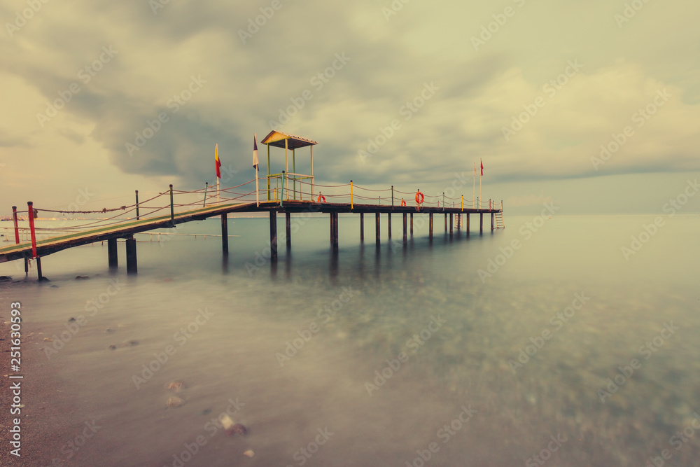 Naklejka premium Beautiful seascape with long gangway. Tropical Resort. Jetty on sunset beach. Turkey. Long exposure shot.