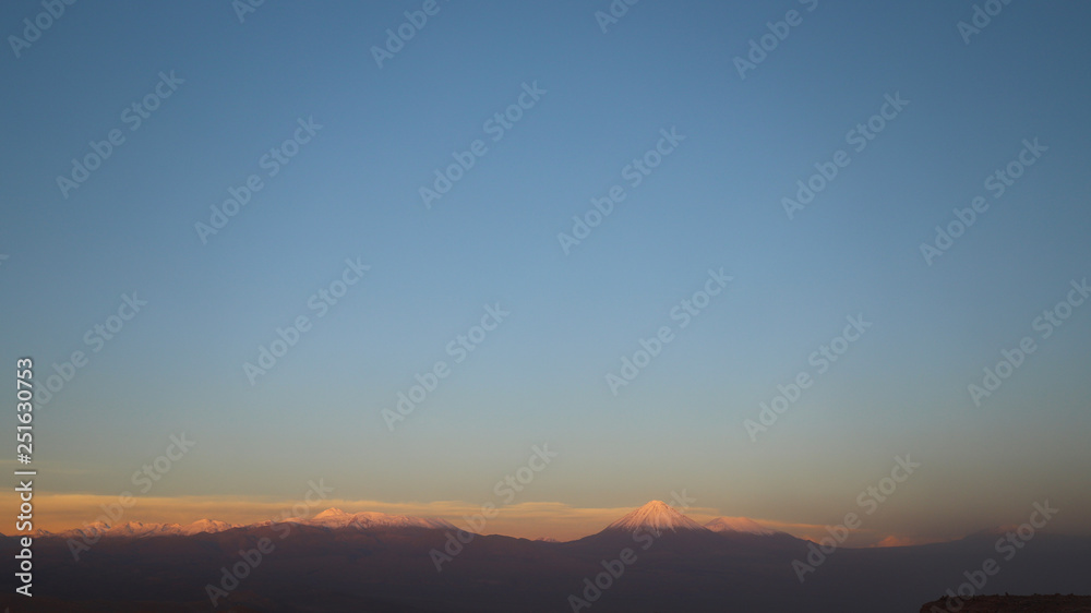 View of the landscape of rocks of the Mars Valley (Valle de Marte) and snow-covered volcanoes at sunset, Atacama Desert, Chile