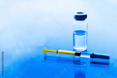 Vials of medication and syringe on a blue glass table with window background