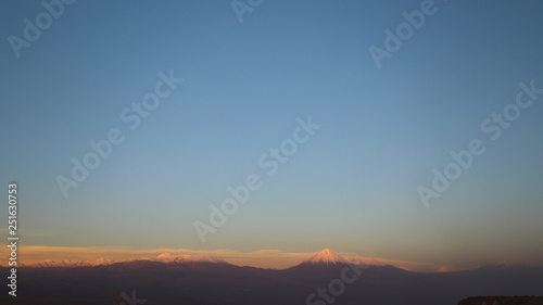 View of the landscape of rocks of the Mars Valley (Valle de Marte) and snow-covered volcanoes at sunset, Atacama Desert, Chile