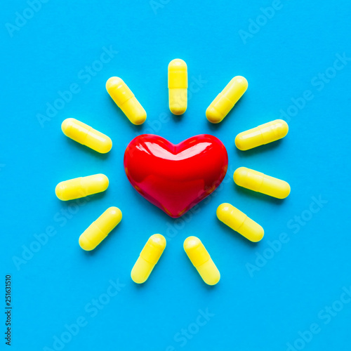 Yellow pills around a red heart fell from a bottle on a blue background. Flat lay, top view. photo