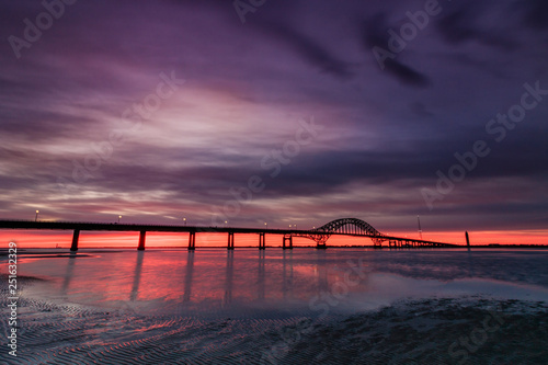 Dramatic deep purple clouds pre dawn over a bridge stretching across a body of water. Fire Island Inlet Bridge - Long Island New York. 