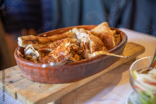 suckling lamb typical style of Segovia province (Castile, Spain, Europe), roasted in large clay oven, served in ceramic tray, on wooden stand, on tablecloth in restaurant photo