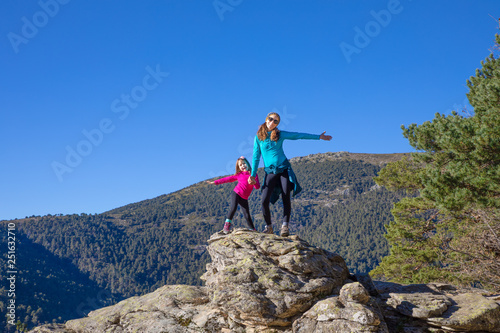 mountaineer happy family (woman and five years old girl) posing on the top of rock in mountain of Fuenfria Valley, in Guadarrama Natural Park (Cercedilla, Madrid, Spain) photo