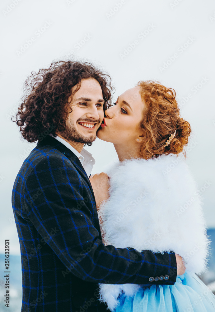  The bride kisses the bridegroom in a cheek in the winter forest.