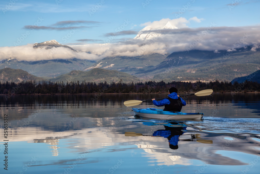Adventurous man kayaking in peaceful water during a cloudy winter day. Taken in Squamish, North of Vancouver, BC, Canada. Adventurous man kayaking in peaceful water during a cloudy winter day. Taken in Squamish, North of Vancouver, BC, Canada.