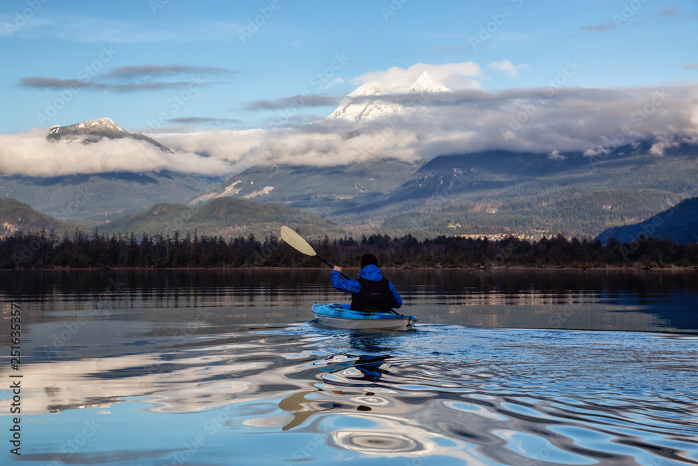 Obraz premium Adventurous man kayaking in peaceful water during a cloudy winter day. Taken in Squamish, North of Vancouver, BC, Canada.