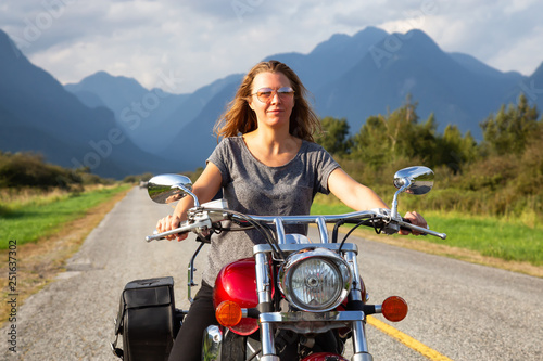Woman riding a motorcycle on a scenic road surrounded by Canadian Mountains. Taken in Pitt Meadows, Greater Vancouver, BC, Canada. photo