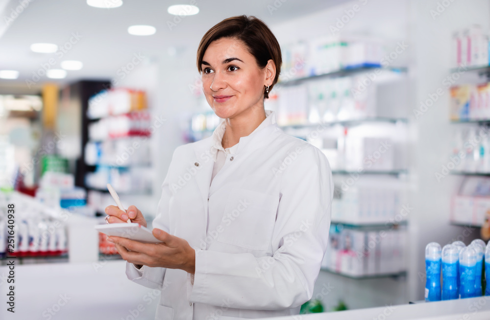Female pharmacist noting assortment of drugs
