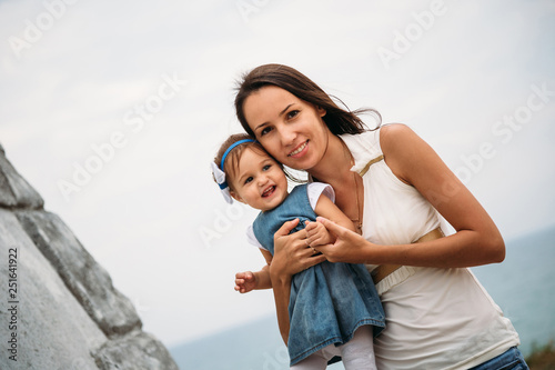 Happy young mother with a small daughter in hands hugging near to the lighthouse, outdoors background © Iryna Budanova