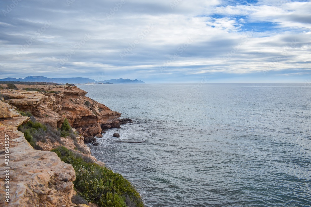 The dry semi-desert of southern Spain meets the blue water of the mediterranean with rocks rising above the water, along the coast of southern Spain